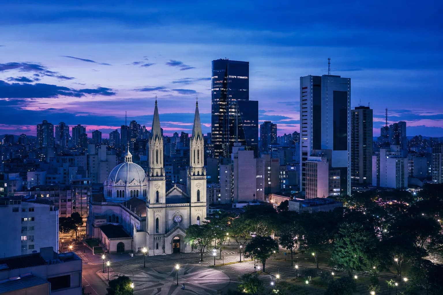 Vista da praça da Catedral de Campinas com torres modernas ao fundo, no fim de tarde