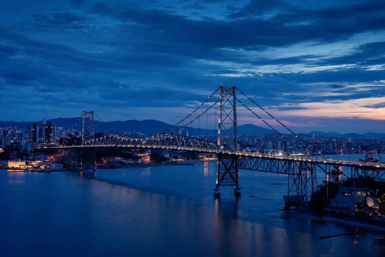 Vista da Ponte Hercílio Luz em Florianópolis ao entardecer, com a baía ao fundo
