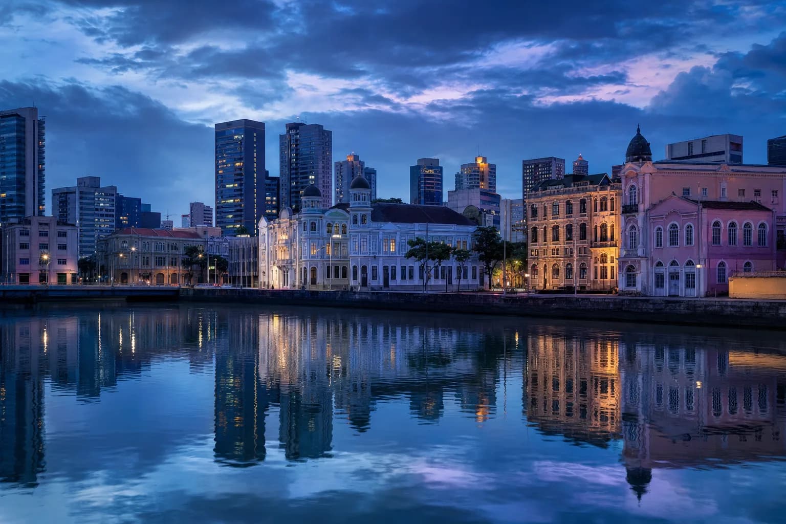 Vista do Recife Antigo à beira-rio, com edifícios históricos e torres modernas ao fundo